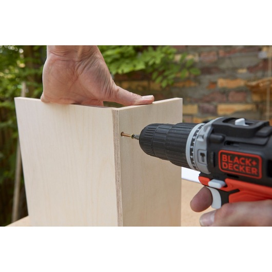 BLACKDECKER BDCHD12S1 cordless drill driving screw into light wood panel outdoors.