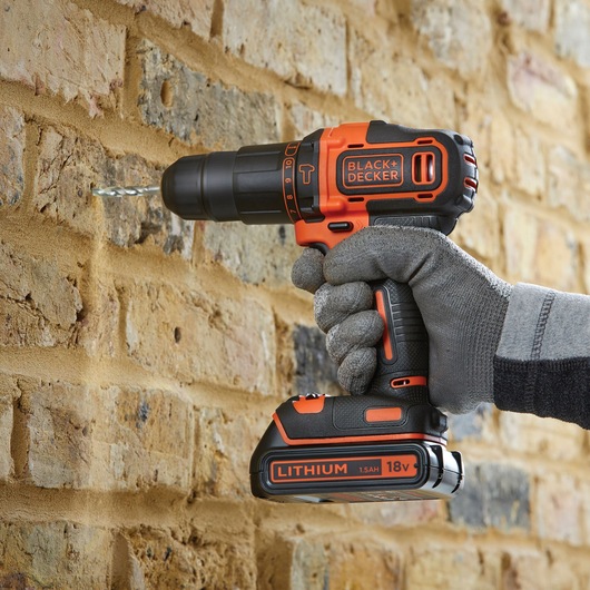 BLACKDECKER BDCHD18S1KA cordless drill being used to drill into a brick wall, close-up side view.