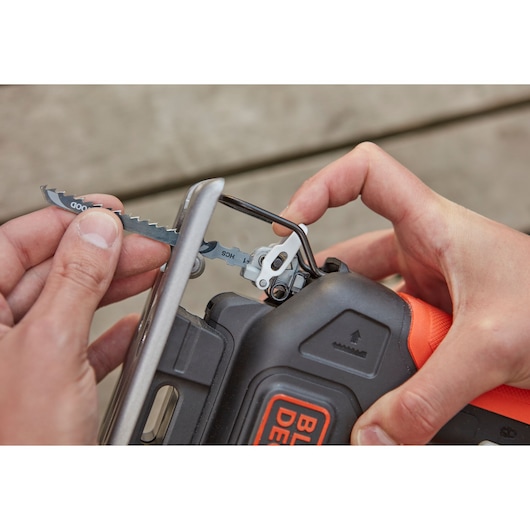 Close-up of a person inserting a saw blade into a BLACKDECKER BDCJS12N jigsaw, showing blade change mechanism.