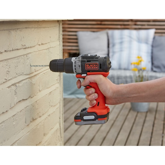 Photo of BLACKDECKER cordless drill BDCK123S2S in use drilling into a brick wall, outdoor setting.