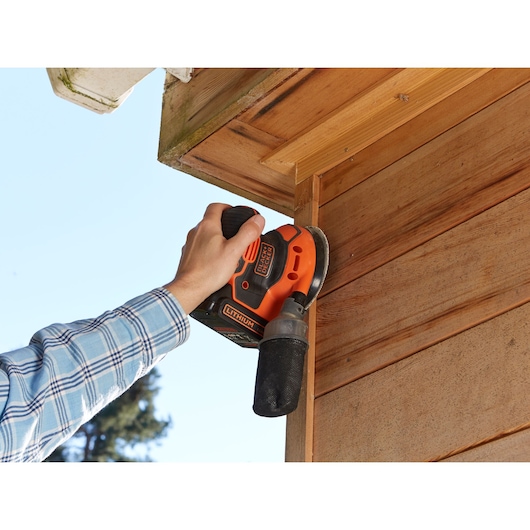BLACKDECKER BDCROS18N cordless sander used on wooden exterior, orange and black tool in hand.