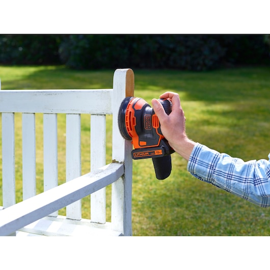 BLACKDECKER BDCROS18 cordless sander sanding a white wooden bench outdoors.