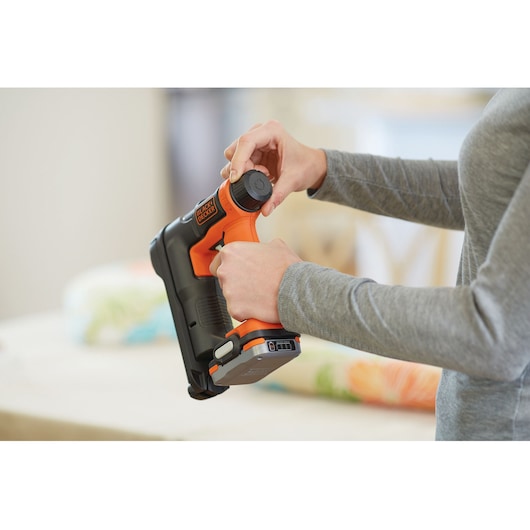 Photo of person adjusting BLACK+DECKER cordless staple gun BDCT12N, showing side view in use.
