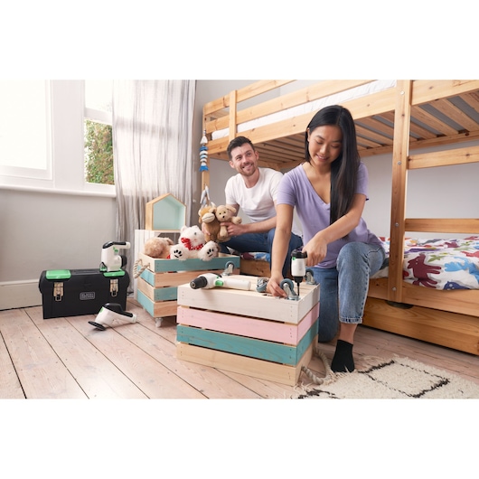BLACK+DECKER BDST60120 toolbox and tools on wooden floor near people building pastel storage crates in a bedroom.
