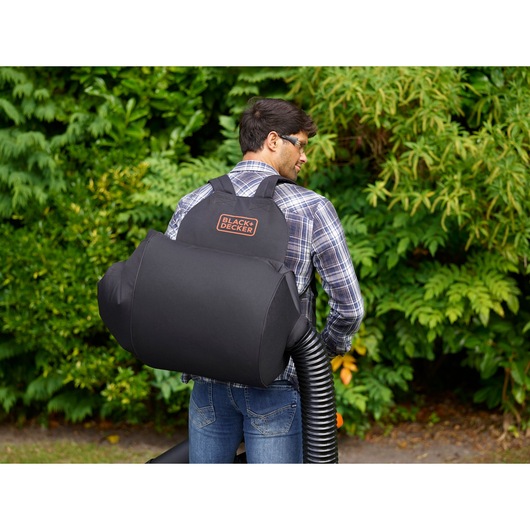 BLACK+DECKER BEBLV290 leaf blower vacuum bag worn on the back in outdoor garden setting.