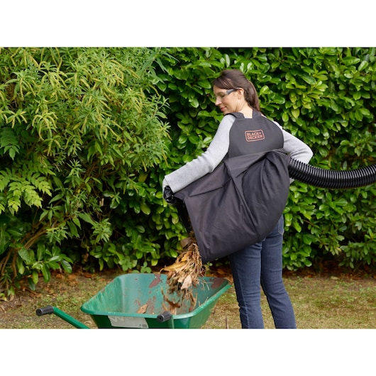 Photo of BLACKDECKER BEBLV290 leaf blower collection bag in use, emptying leaves into a wheelbarrow outdoors.