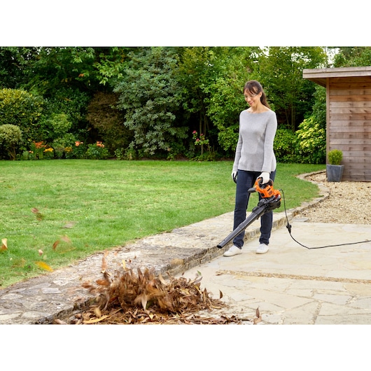 BLACKDECKER BEBLV300 leaf blower in use outdoors, blowing leaves from stone patio.