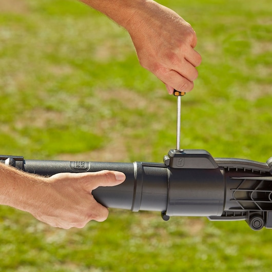 Photo of hands assembling BLACKDECKER BEBLV300 blower tube outdoors with screwdriver.
