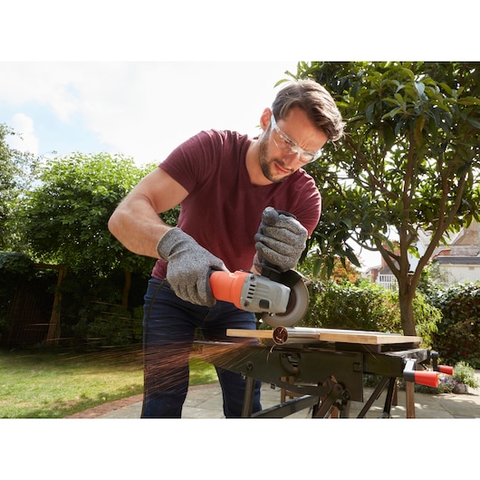 Photo of BLACKDECKER BEG010 angle grinder cutting metal outdoors, sparks flying, operator wearing gloves.