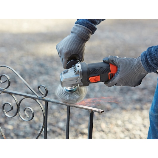 BLACKDECKER BEG220K angle grinder in use on metal fence, close-up with sparks and gloves visible.