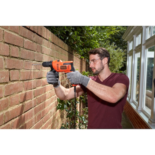 BLACKDECKER BEH200K corded drill in use drilling into outdoor brick wall.
