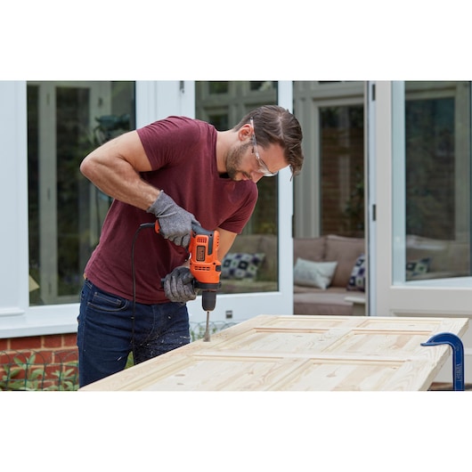 BLACKDECKER BEH200K corded drill in use on a wooden door, worn with gloves in an outdoor setting.