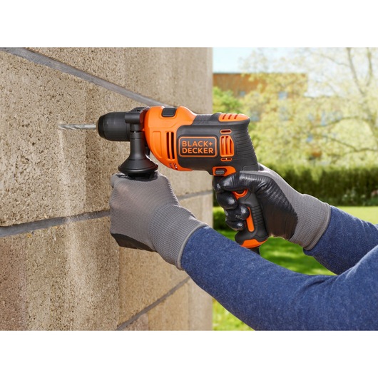 BLACK+DECKER BEH710SA32 hammer drill in use, drilling into exterior brick wall, operator wearing gloves.