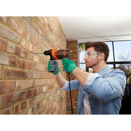 BLACKDECKER BEH710SA32 corded drill used on brick wall, person wearing gloves, indoor setting.
