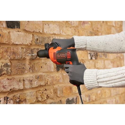 BLACK+DECKER BEH710 corded hammer drill in use drilling into brick wall, black and orange design.