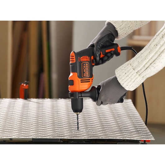 Photo of BLACKDECKER BEH710 hammer drill in use drilling into metal sheet, worker wearing gloves.