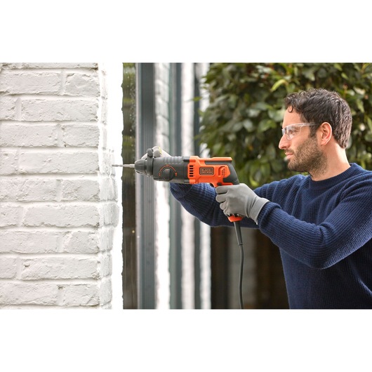 BLACKDECKER BEHS01K corded hammer drill used on white brick wall, orange and black design, side view.