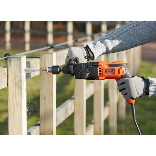 BLACKDECKER BEHS01K corded hammer drill in use drilling into wooden fence outdoors.