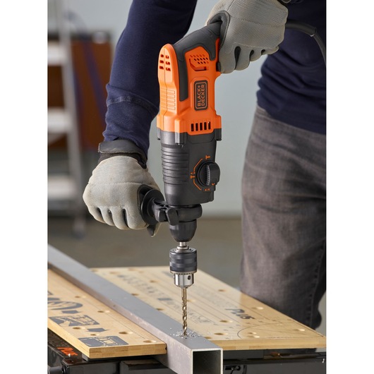 BLACKDECKER BEHS01 hammer drill in use on metal, orange and black body, user wearing gloves.