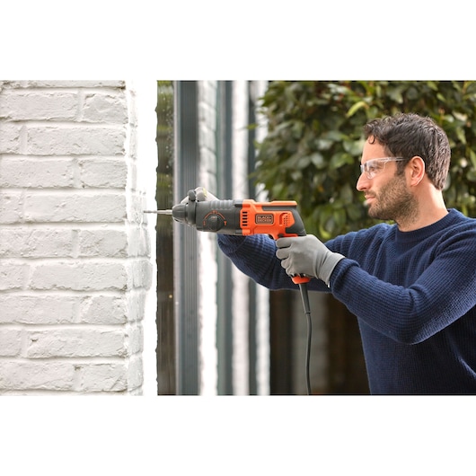 BLACKDECKER BEHS01 corded hammer drill in use on white brick wall, product photography.