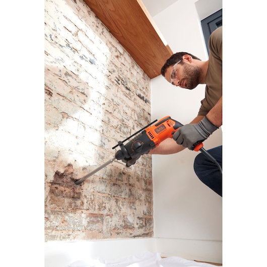 BLACKDECKER BEHS01 rotary hammer drill used on a brick wall, side angle, orange and black color.
