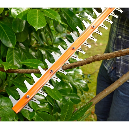 BLACKDECKER BEHT251 hedge trimmer cutting a thick branch among green leaves outdoors.