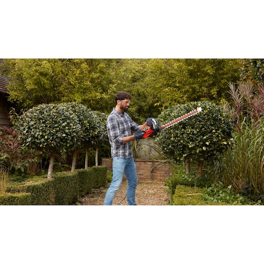 BLACKDECKER hedge trimmer BEHTS451 in use trimming bushes in a garden.