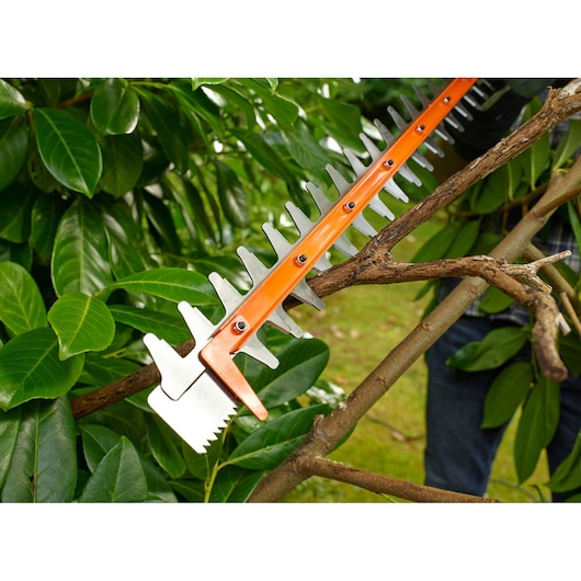BLACKDECKER BEHTS501 hedge trimmer cutting thick branch outdoors, close-up of blade and plants.
