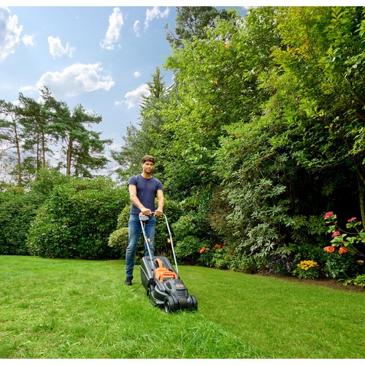BLACKDECKER BEMW351 lawn mower used outdoors on grass, garden background, side angle.