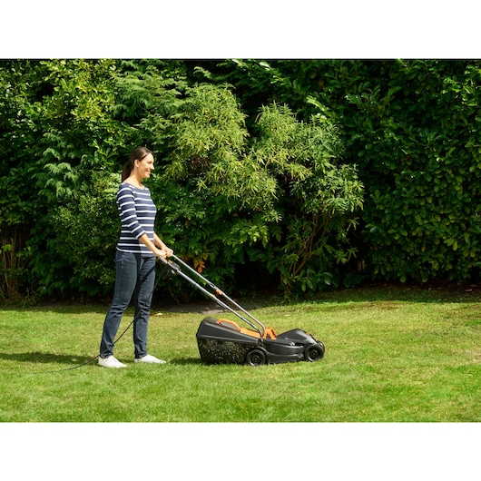 Photo of person using BLACKDECKER BEMW351 electric lawn mower on grass in a garden setting.