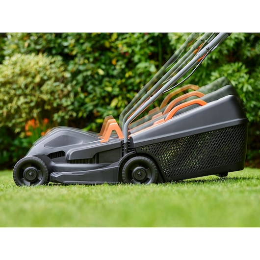 BLACKDECKER BEMW351 lawn mower with adjustable handle on grass, side profile, garden background.