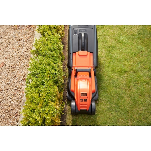 BLACK+DECKER BEMW451BH orange lawn mower top-view trimming grass along hedge.