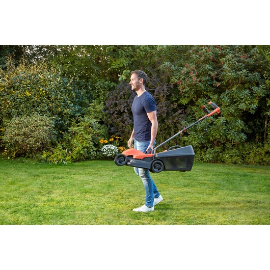 BLACKDECKER BEMW451BH lawn mower in use, carried by a person on a green garden lawn.