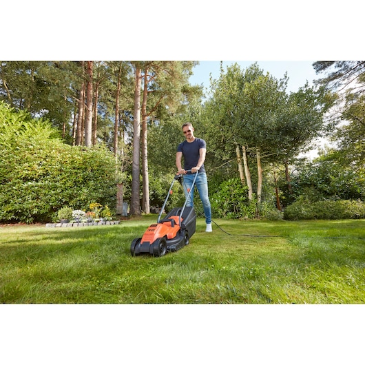 BLACKDECKER BEMW451 corded lawn mower in use on grass in a garden setting.