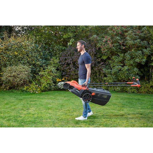 BLACKDECKER BEMW471BH lawn mower carried by person in garden setting.