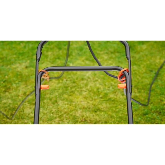 BLACKDECKER BEMW481ES lawn mower handle close-up with orange lever clips on green grass background.