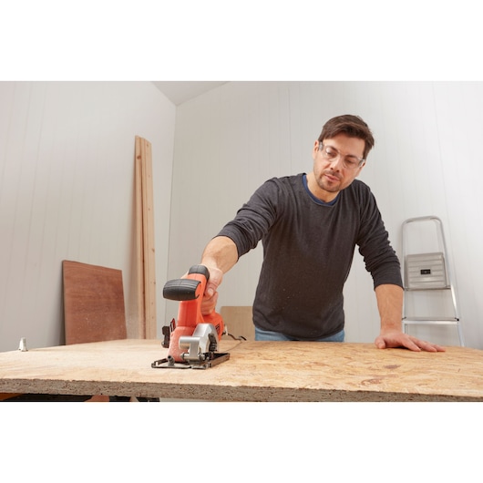 BLACKDECKER BES510K compact circular saw in use cutting plywood on a workbench, indoor workspace setting.