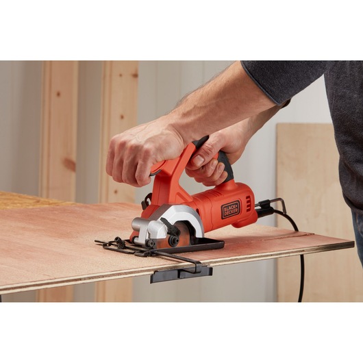 Person using BLACK+DECKER BES510 compact circular saw to cut plywood, handheld power tool in action.
