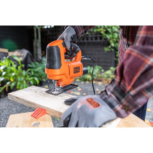 BLACKDECKER BES602 jigsaw in use cutting wood, user wearing gloves outdoors.