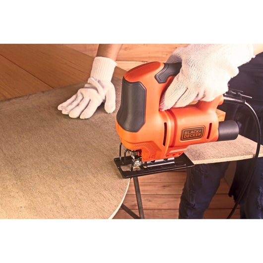 Photo of BLACK+DECKER BES603 jigsaw cutting wood, person wearing white gloves holding tool.