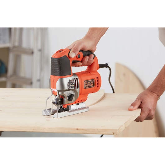 BLACK+DECKER BES610K jigsaw with orange and black body shown cutting curved line in wooden board.
