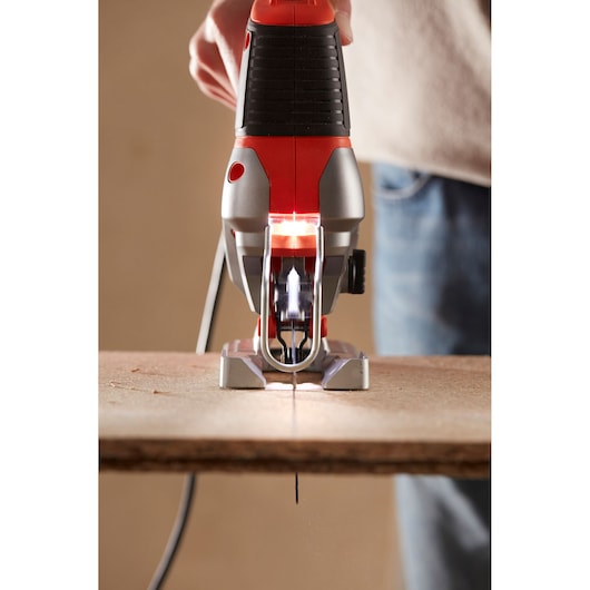 BLACKDECKER BES610K jigsaw in use, front angle, cutting wood with blade visible and LED light on.
