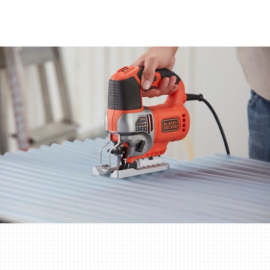 BLACK+DECKER BES610K jigsaw in use cutting corrugated metal, photography showing orange and black design.