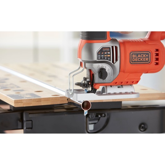 Photo of BLACK+DECKER BES610 jigsaw cutting a metal pipe on a workbench, close-up angle.