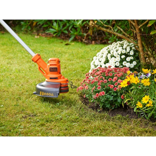 Photo of BLACK+DECKER BESTA525 grass trimmer in use edging a flower bed with colorful flowers in a garden.