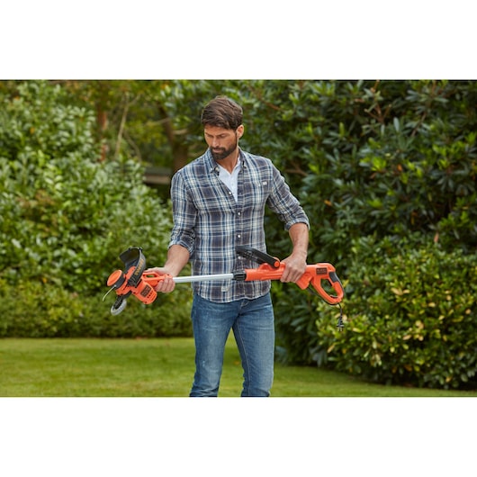Photo of person holding BLACKDECKER BESTA530CM orange grass trimmer with cord in a garden setting.