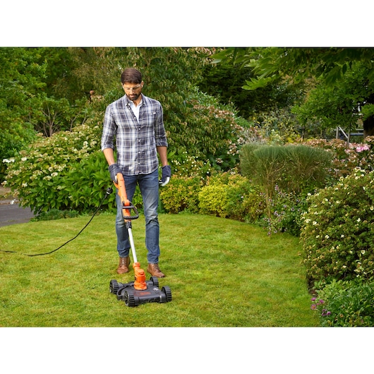 BLACKDECKER BESTA530CM corded lawn mower in use on green grass in garden setting.