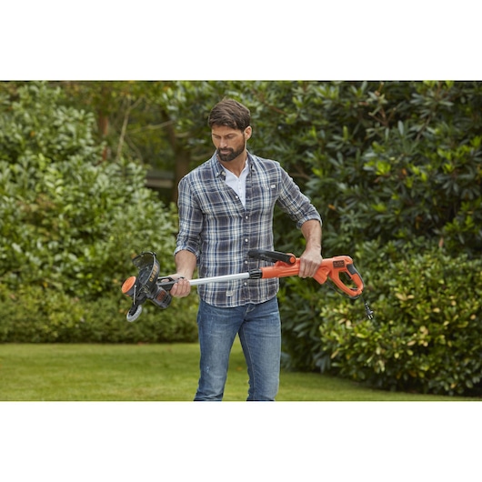 BLACKDECKER BESTE630 grass trimmer held outdoors, orange and black with telescopic shaft.
