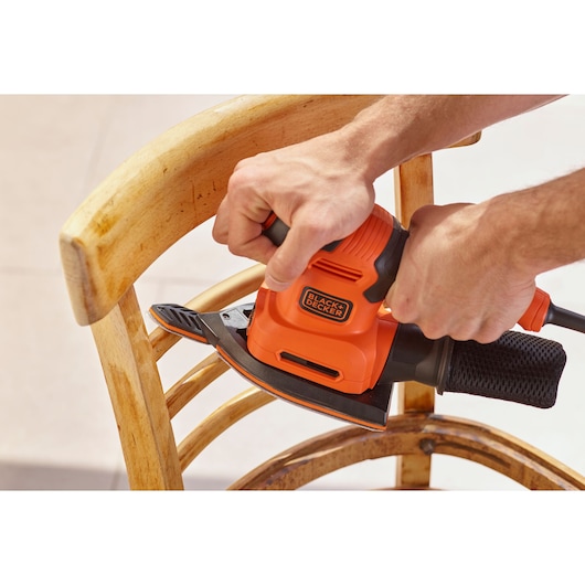 BLACKDECKER BEW200 orange sander in use on wooden chair, close-up view.