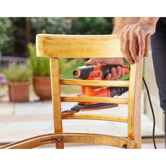 BLACKDECKER BEW200 hand sander used on wooden chair outdoors.